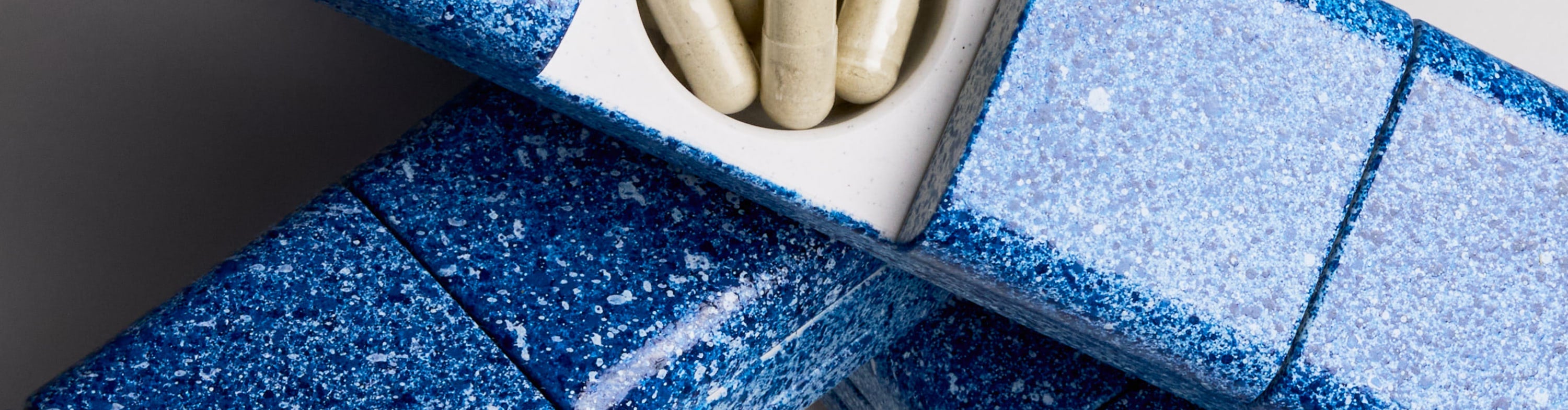 Close-up of the AndAgain Hand-Painted Edition pill case in Blueberry—vibrant speckled finish with capsules visible inside open compartment.