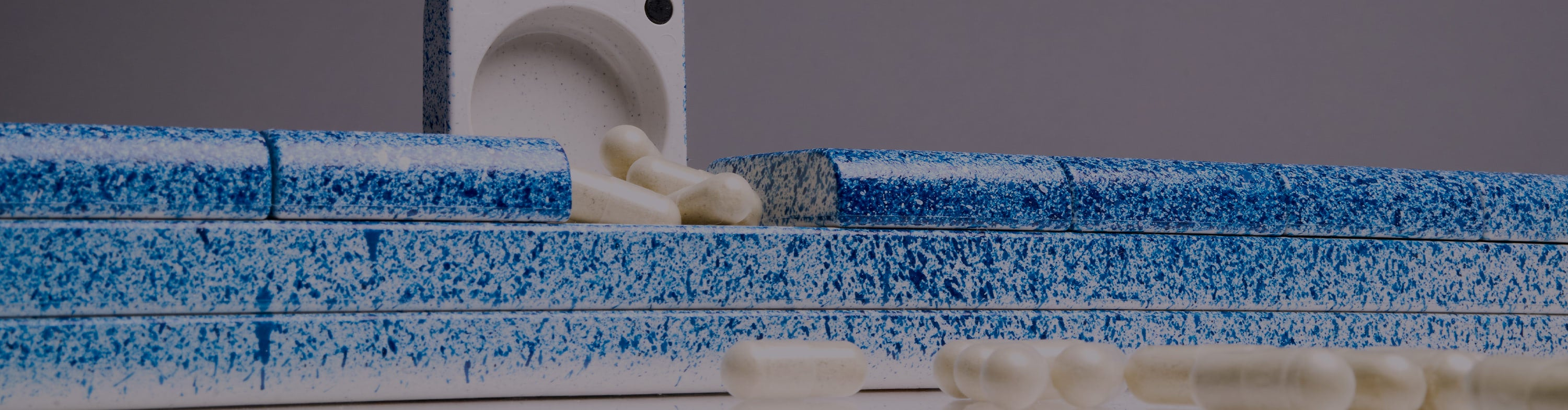 AndAgain Hand-Painted Edition pill case in Blueberry, with capsules spilling from an open compartment—bold speckled design meets everyday function.