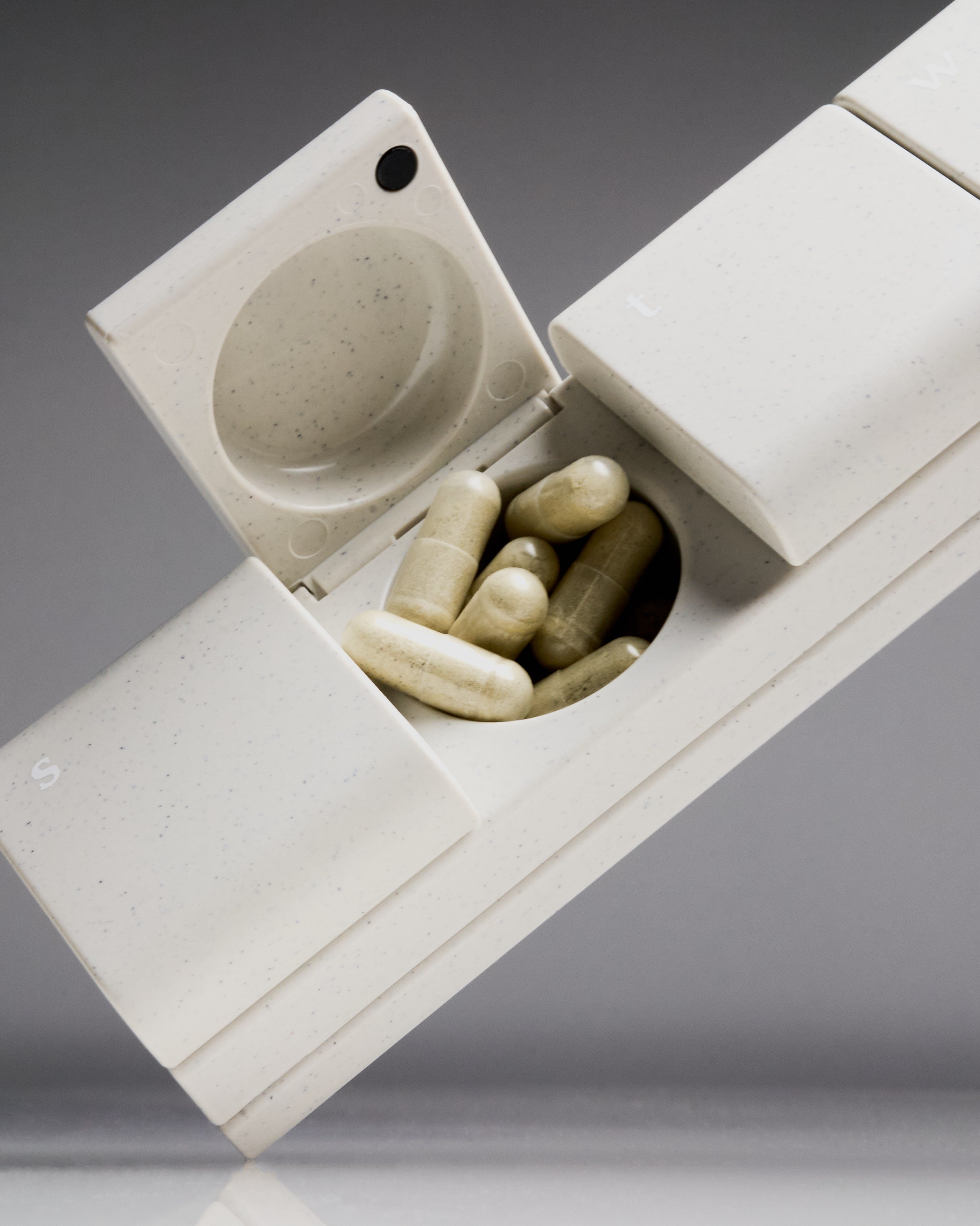 Sleek and modern AndAgain 7-Day Pill Organizer in speckled cream finish, with open lid revealing supplement capsules—designed for daily wellness routines.