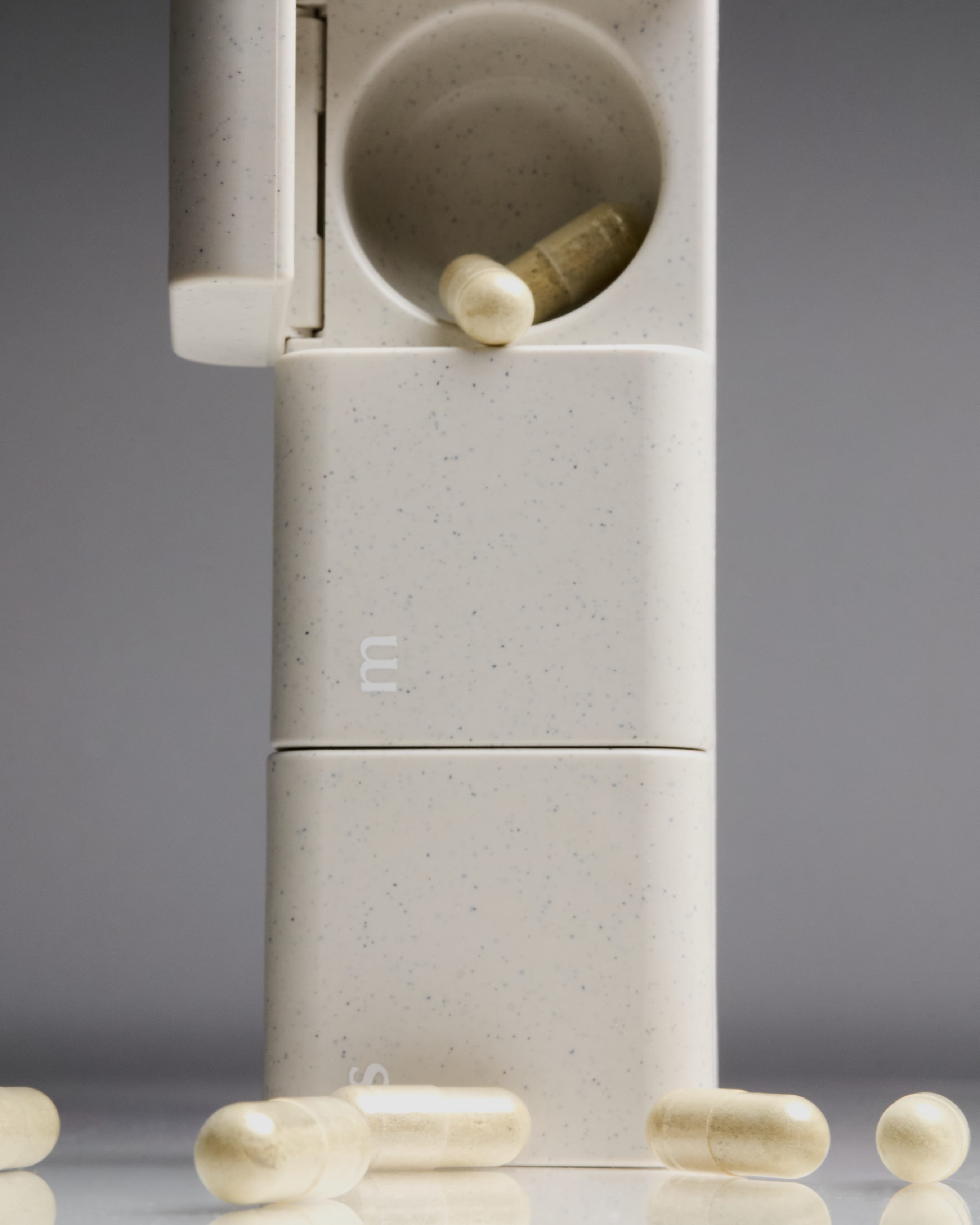 Minimalist and sleek AndAgain supplement pill cases in original finish stacked, showing weekday labels and clean speckled surface—ideal for organized wellness routines.