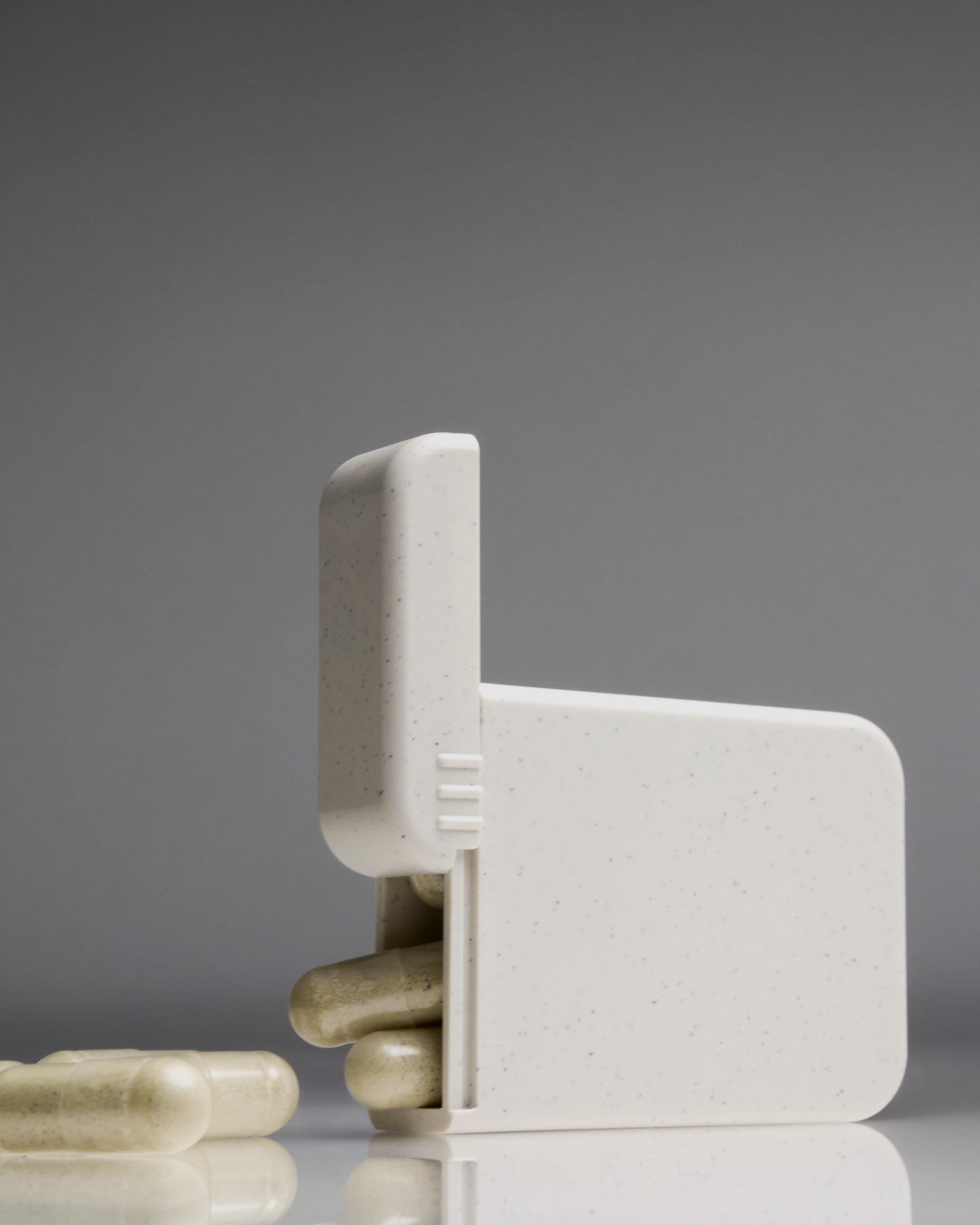 Compact AndAround pill case dispensing capsules onto seamless surface—modern travel-friendly design for daily vitamins or supplements.