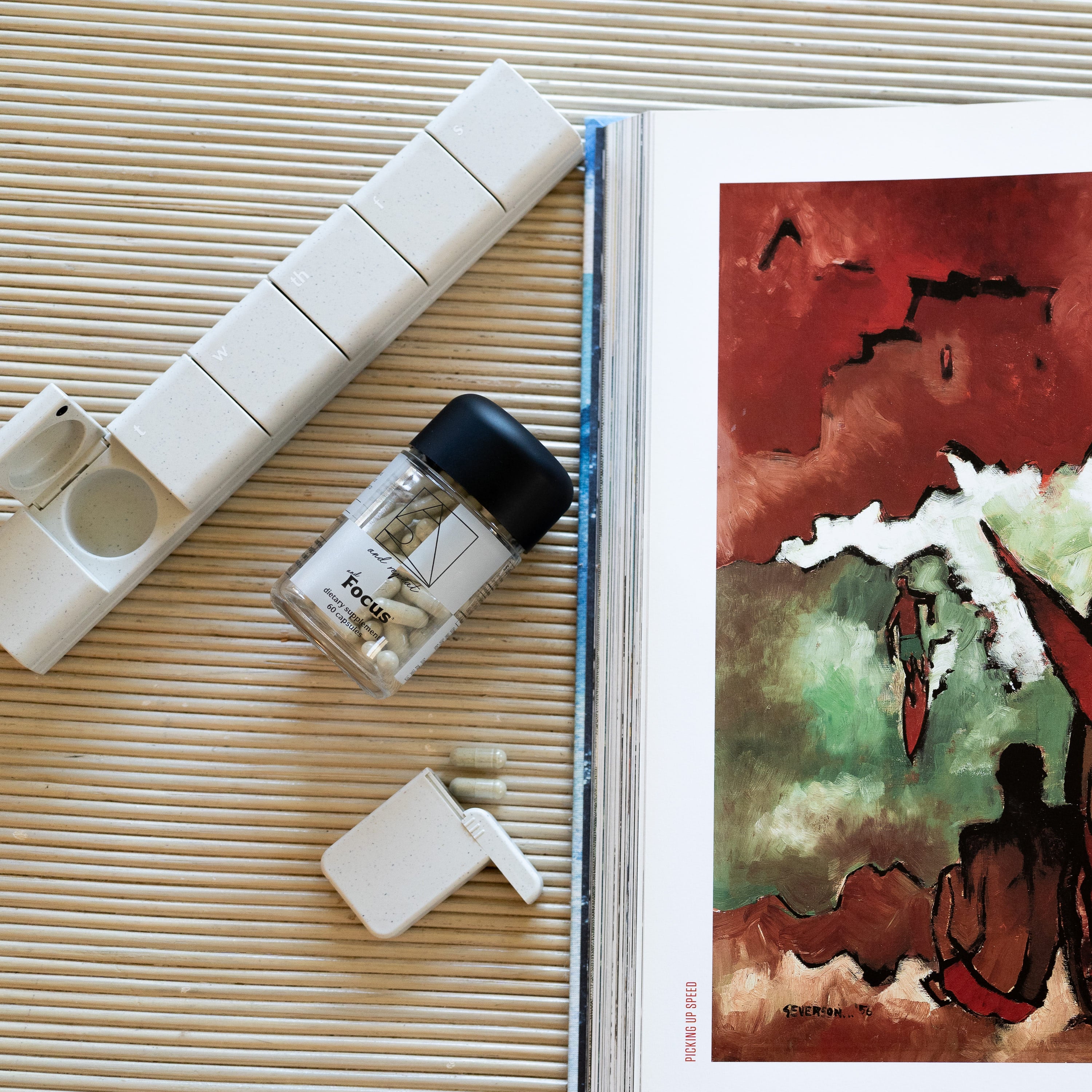 AndBundle 2.0 displayed on a table with a book, featuring the AndAgain 7-Day Pill Case, AndFocus supplement, and AndAround travel case for on-the-go wellness.