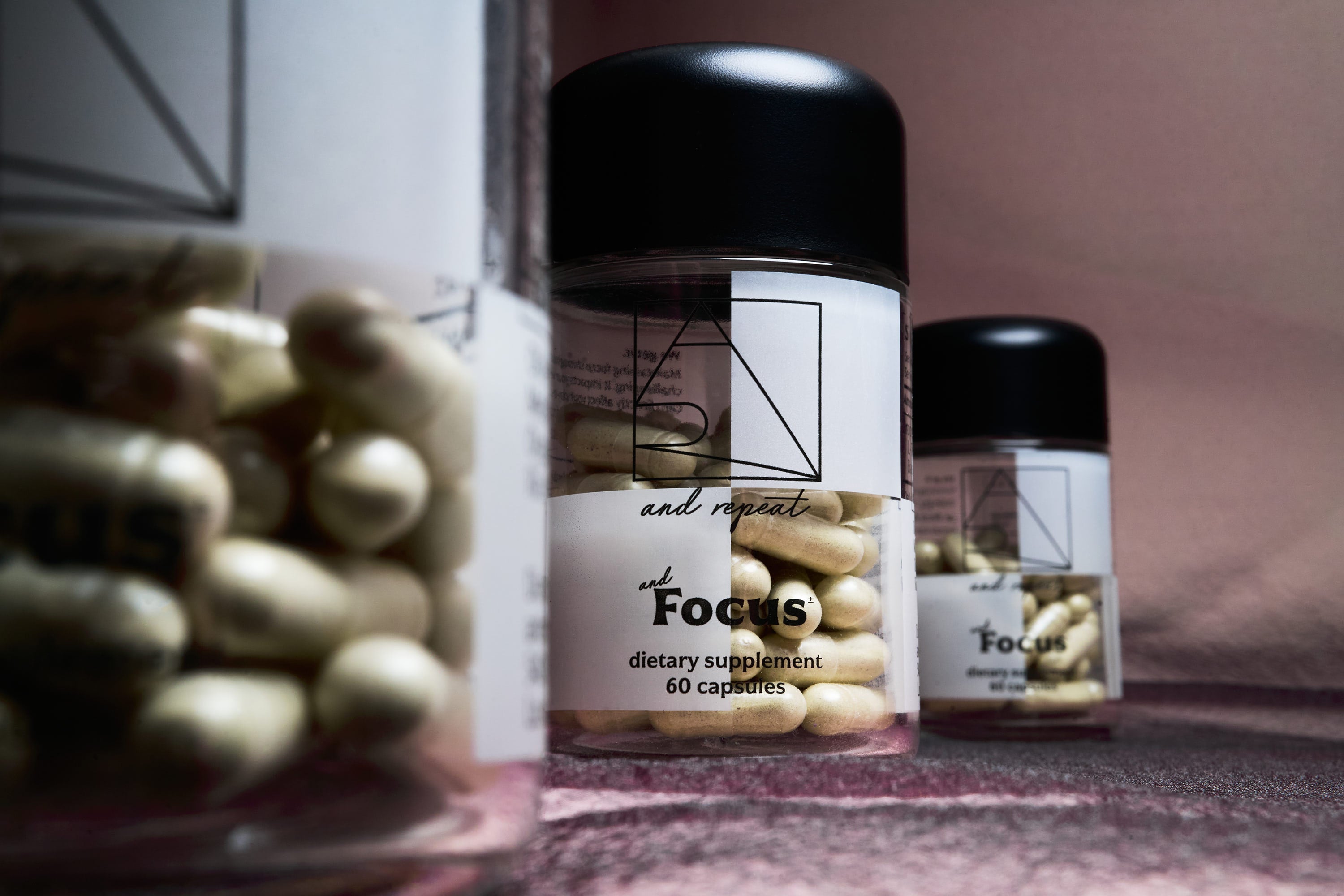 Three And Repeat AndFocus dietary supplement bottles with 60 capsules arranged on a soft pink fabric surface.