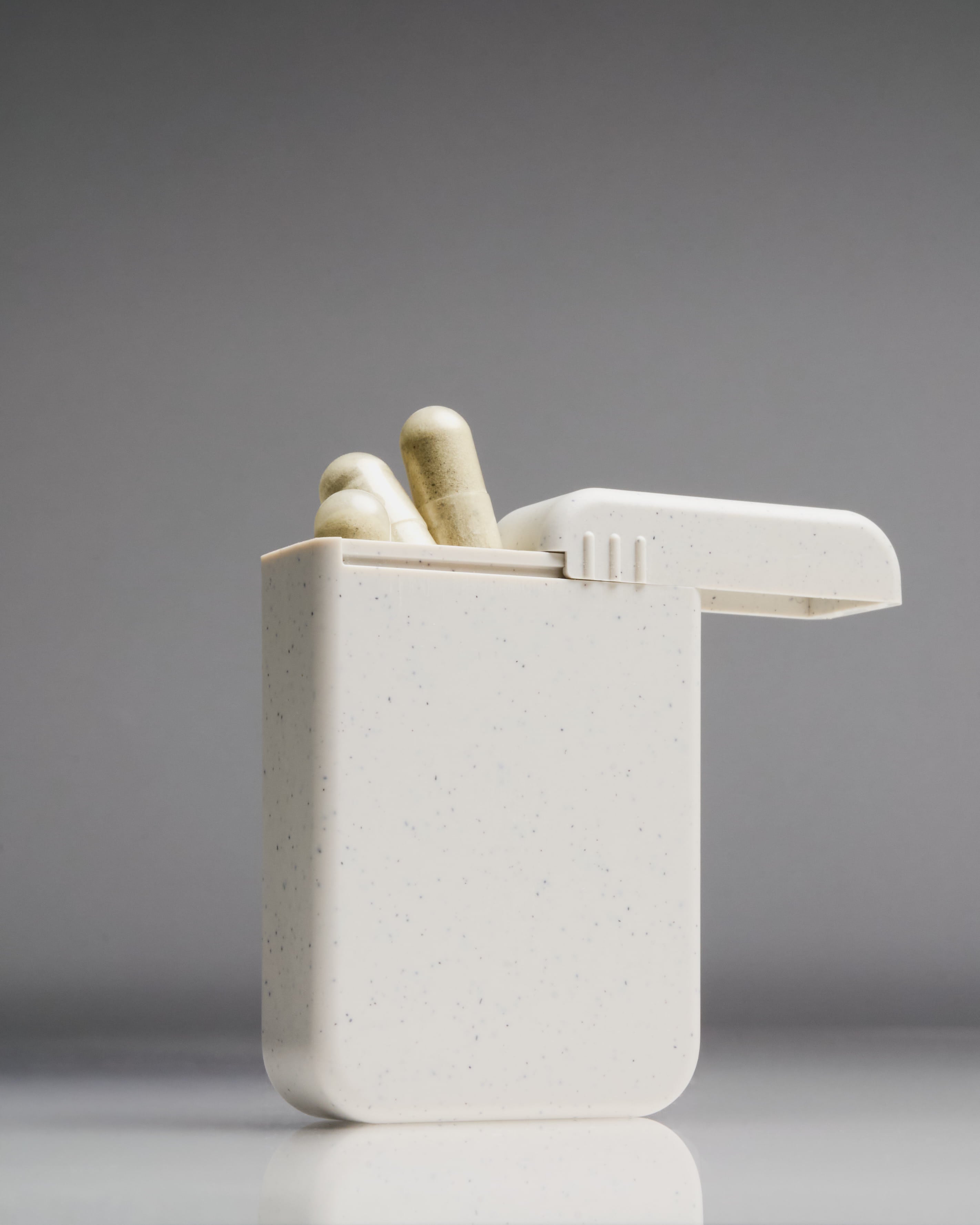 Sleek and minimalist AndAround travel pill case with flip-top lid open and capsules inside—designed for on-the-go supplement routines.