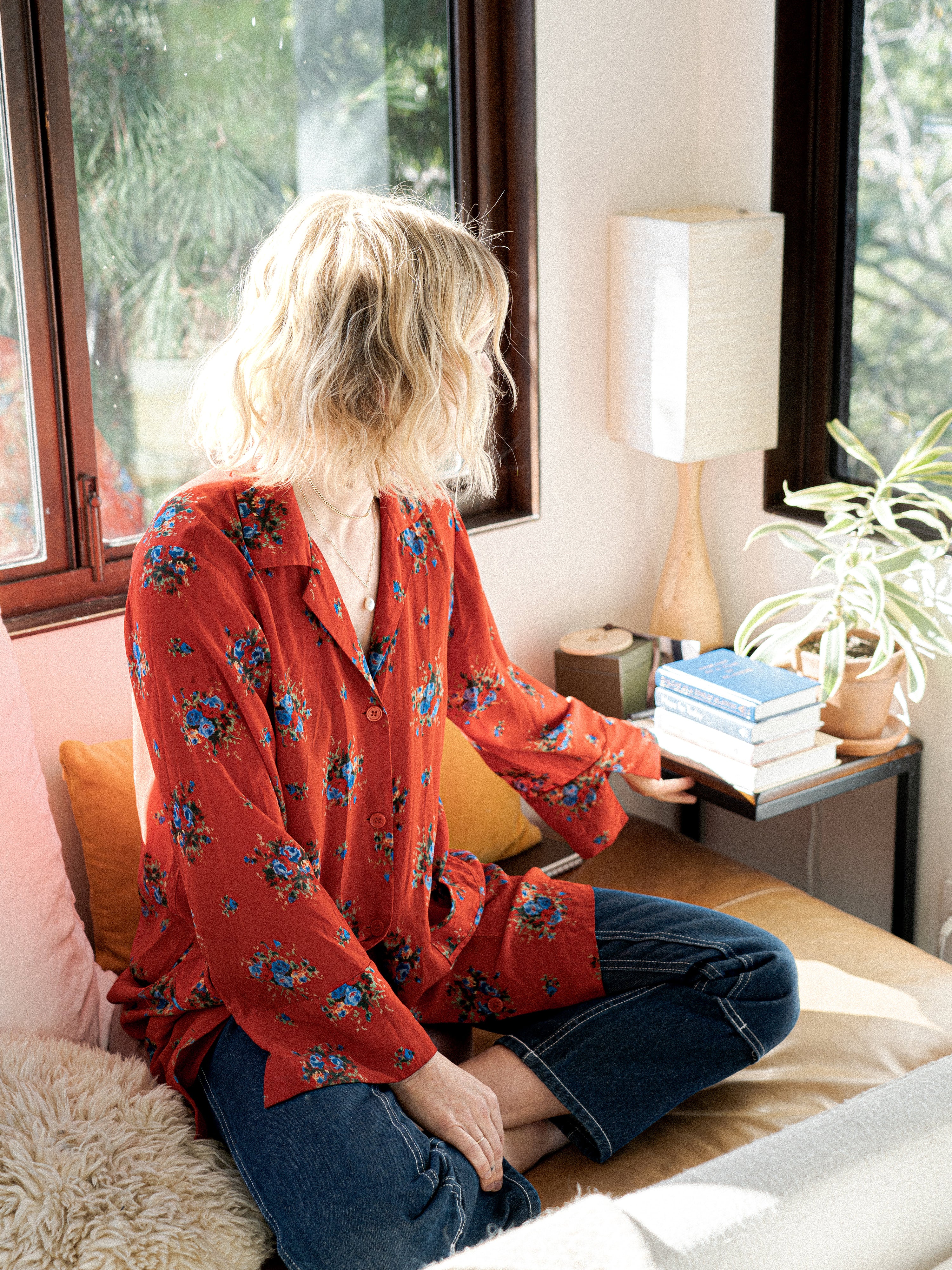 Kacie Carter, chef and co-founder of Honey Hi and holistic nutritionist sitting on a chair in her living room, reaching for books on a side table