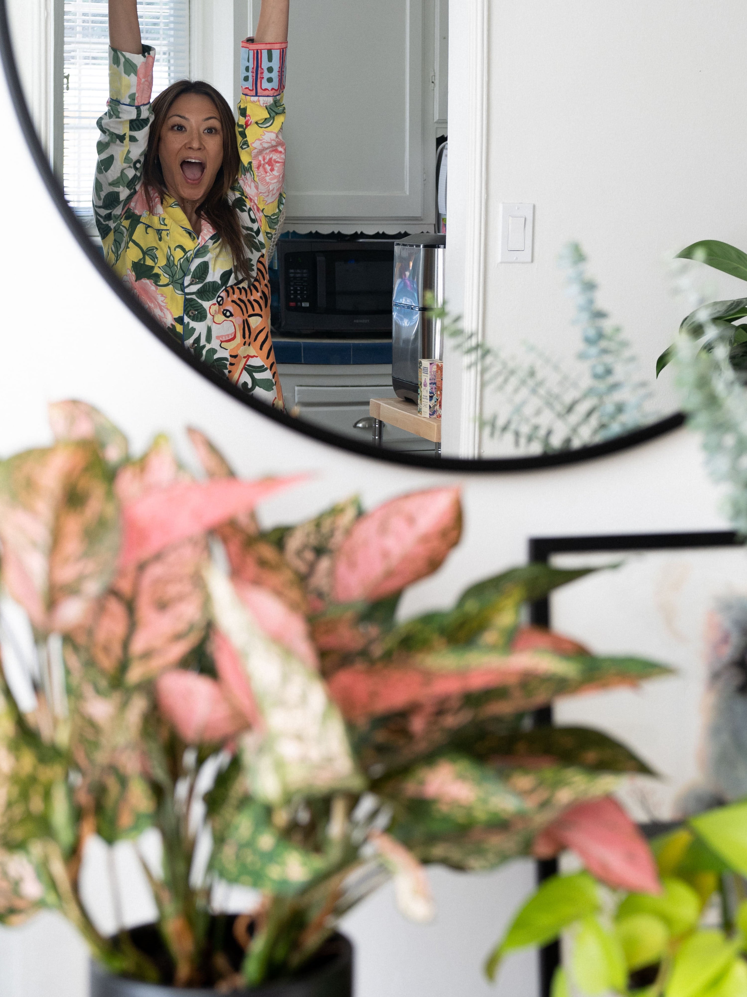 Aesthetician Sora Connor looking at herself in the mirror with raised hands and smiling big.