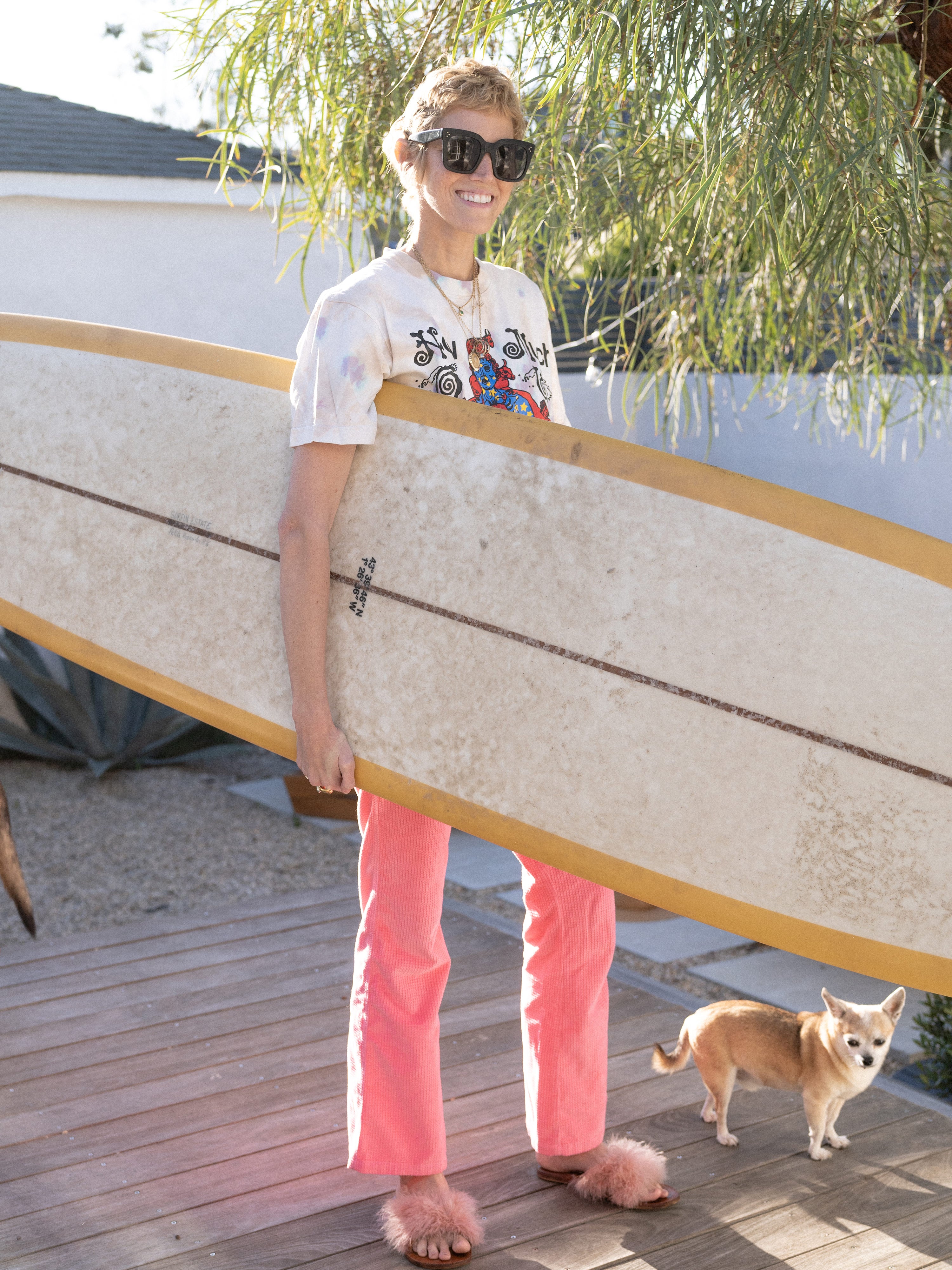 Fashion and beauty journalist, and founder of Herbs for Relaxation, Sue Williamson standing outside while holding her surfboard