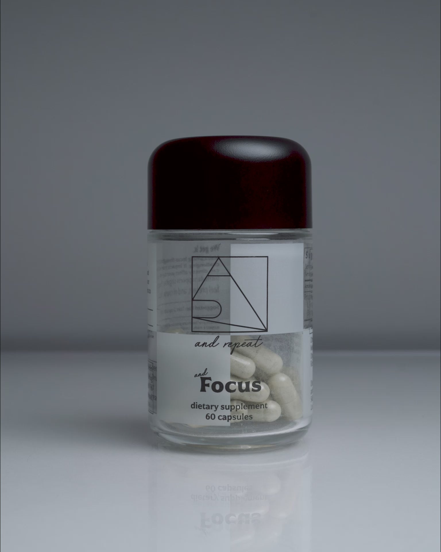 Hand picks up AndFocus supplement bottle, opens it, pours capsules into palm, then closes and sets it back down—shot on a clean, seamless background.