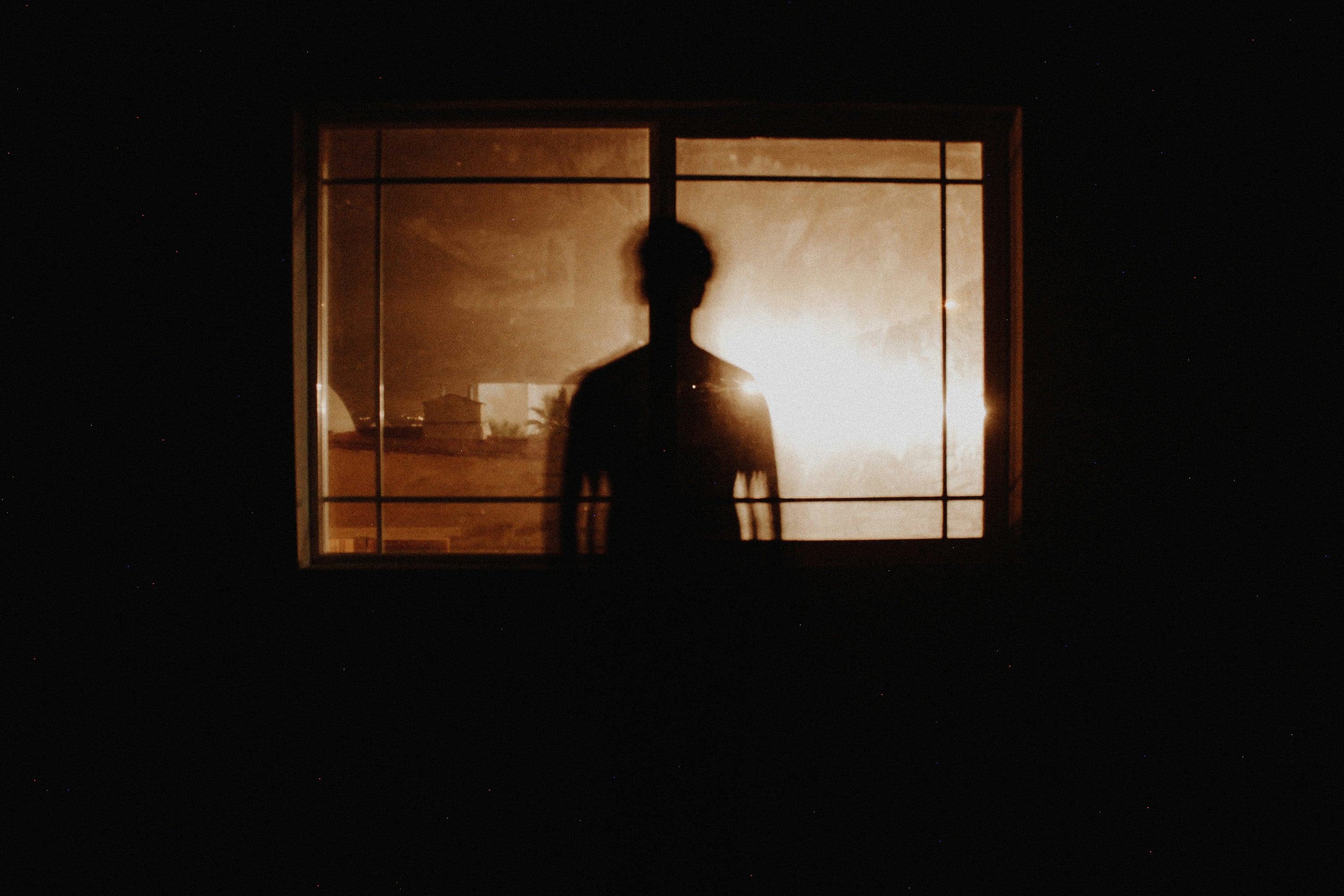 Photo of a person at night behind a window with a backlight that is bright and warm, making it a bit abstract, conceptually the link between focus and mental health