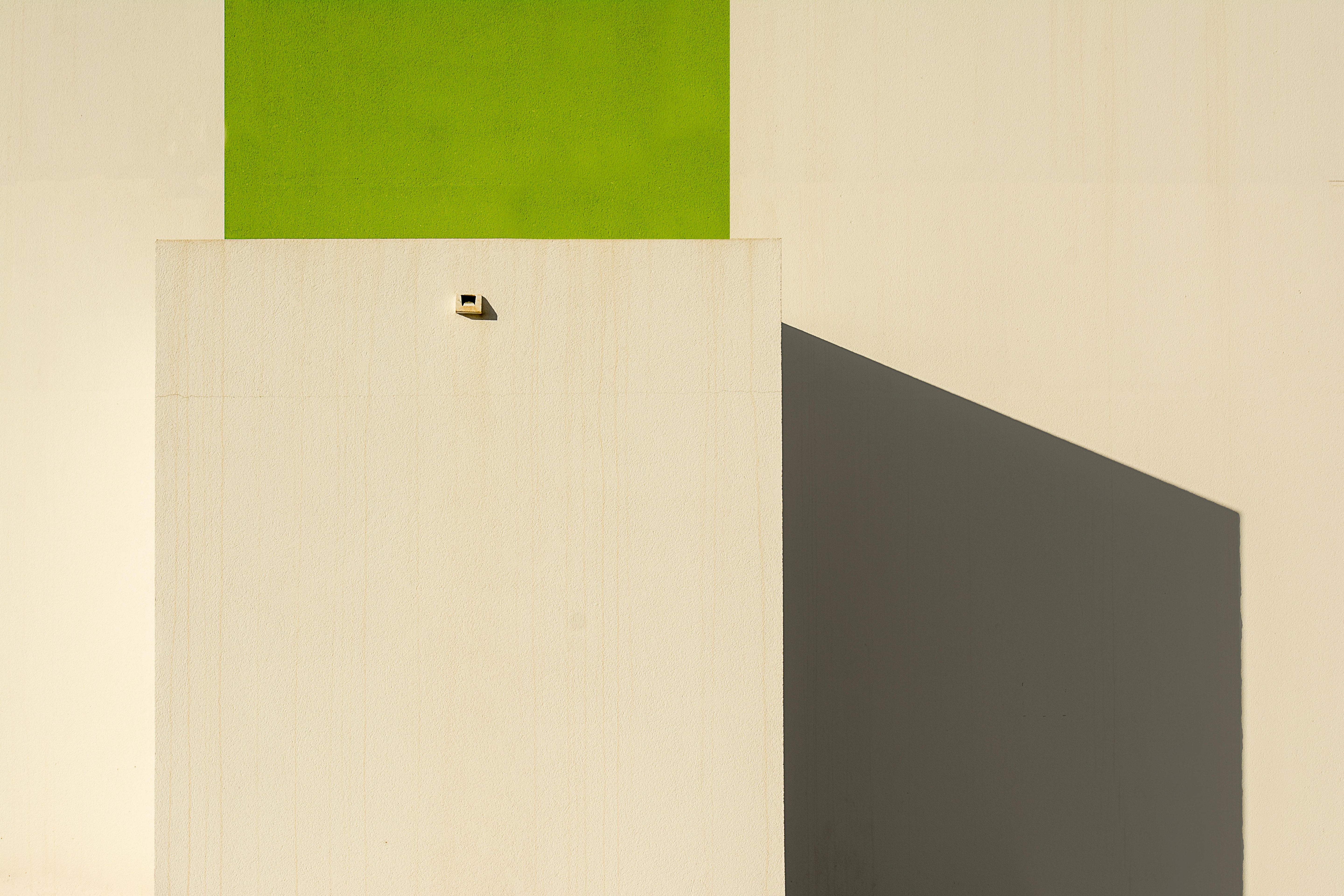 Minimalist architectural facade with a bold green block and sharp geometric shadows in afternoon light.