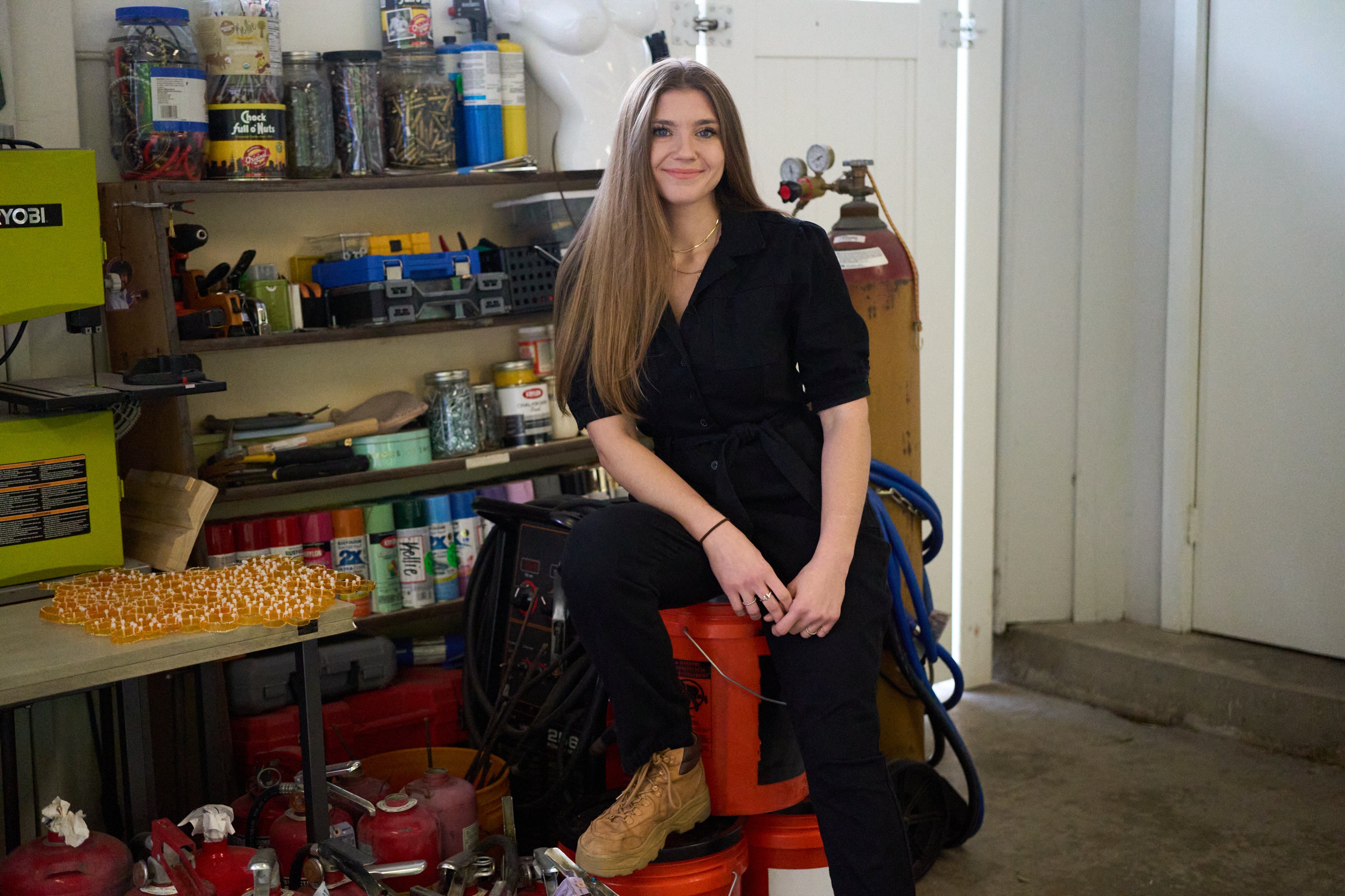 Artist Kellie Gillespie sitting in her studio with her piece Over/Medicated/Under sitting on the table next to her