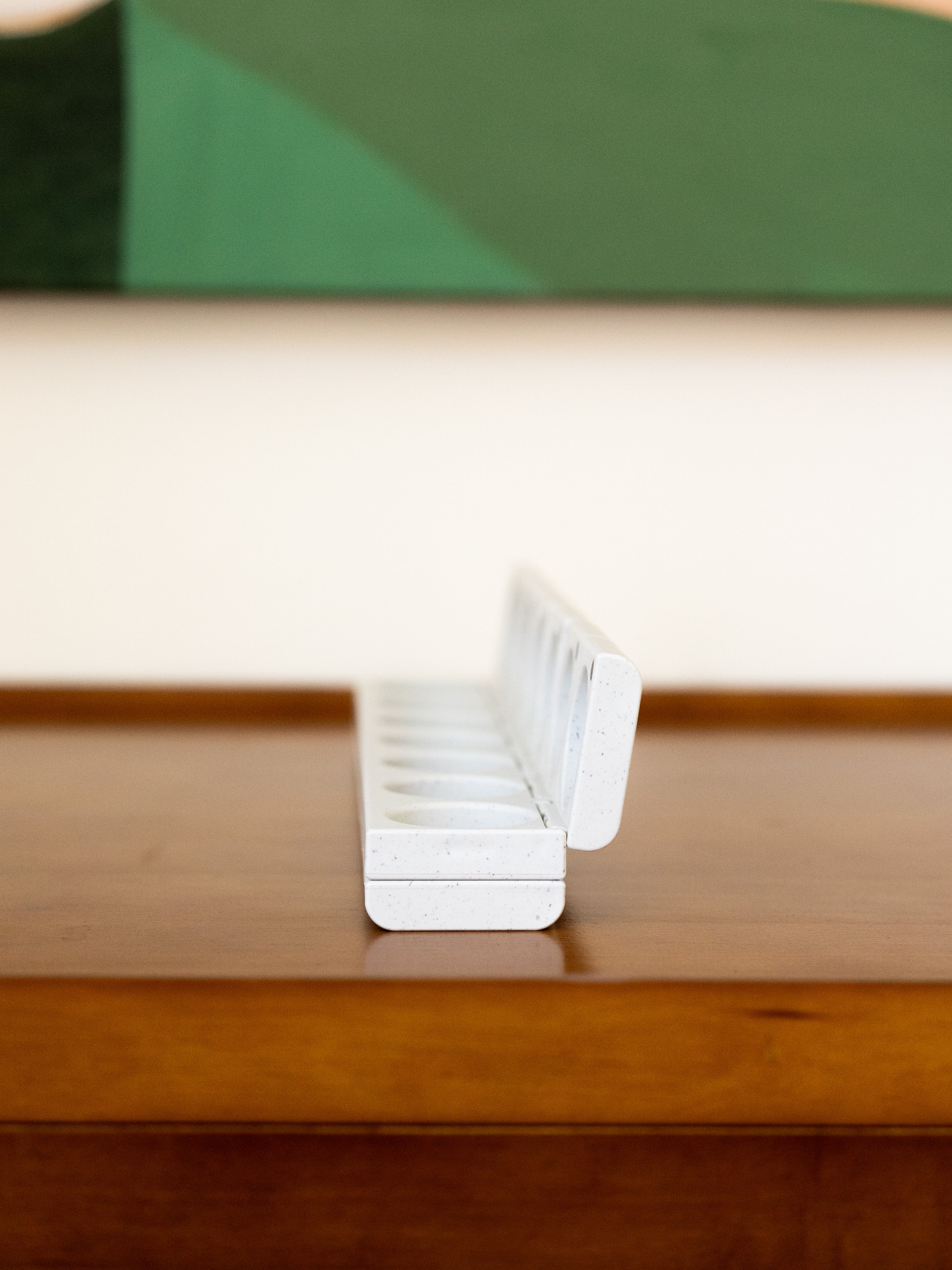 AndAgain 7-Day Pill Case with open lids, resting on a wooden table with artwork in the background—designed for stylish, organized wellness.